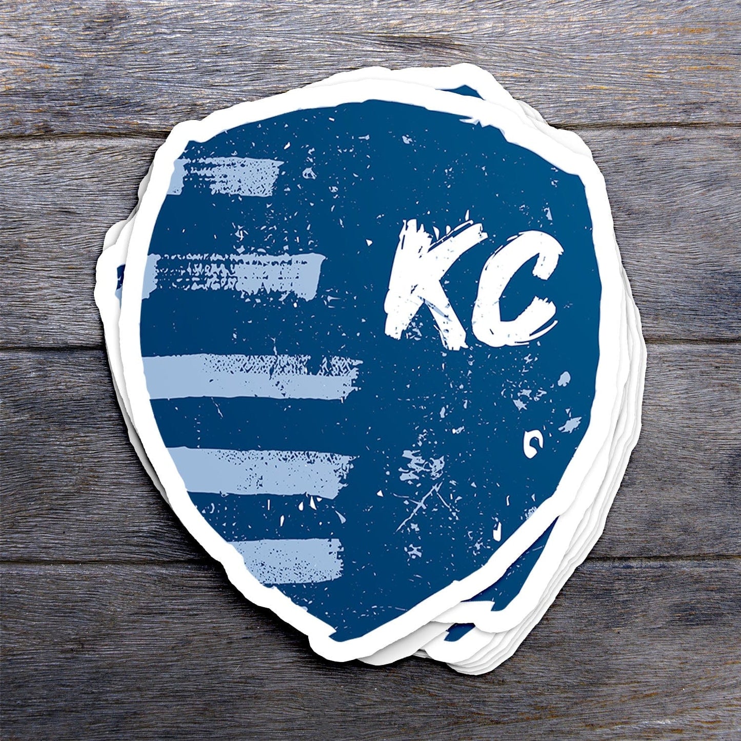 KC Swag Sporting Kansas City powder, navy, white Painted Shield vinyl die cut decal sticker stack on dark wood table