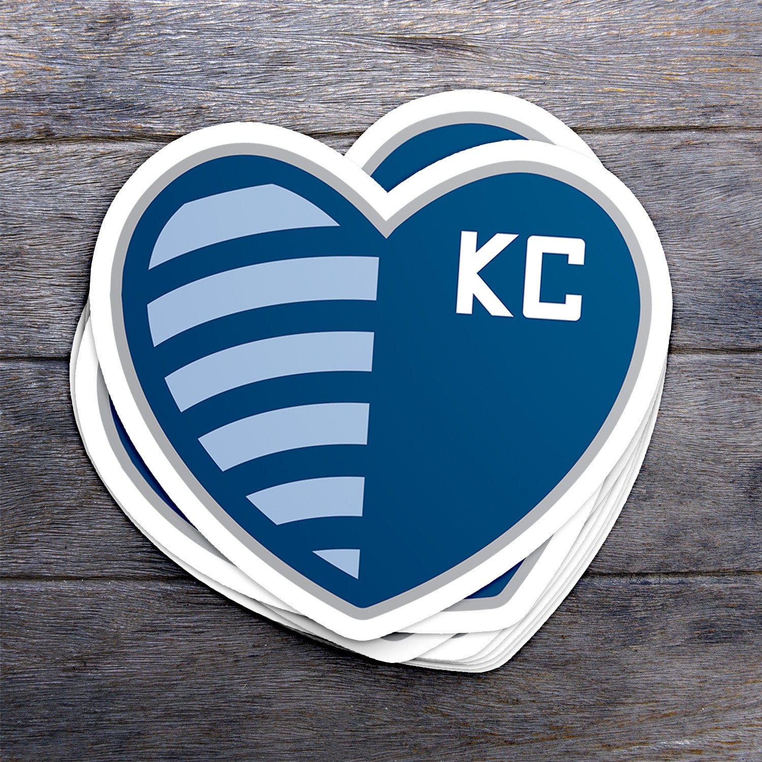 KC Swag Sporting Kansas City powder, navy, silver Shield Heart vinyl die cut decal sticker stack on dark wood table