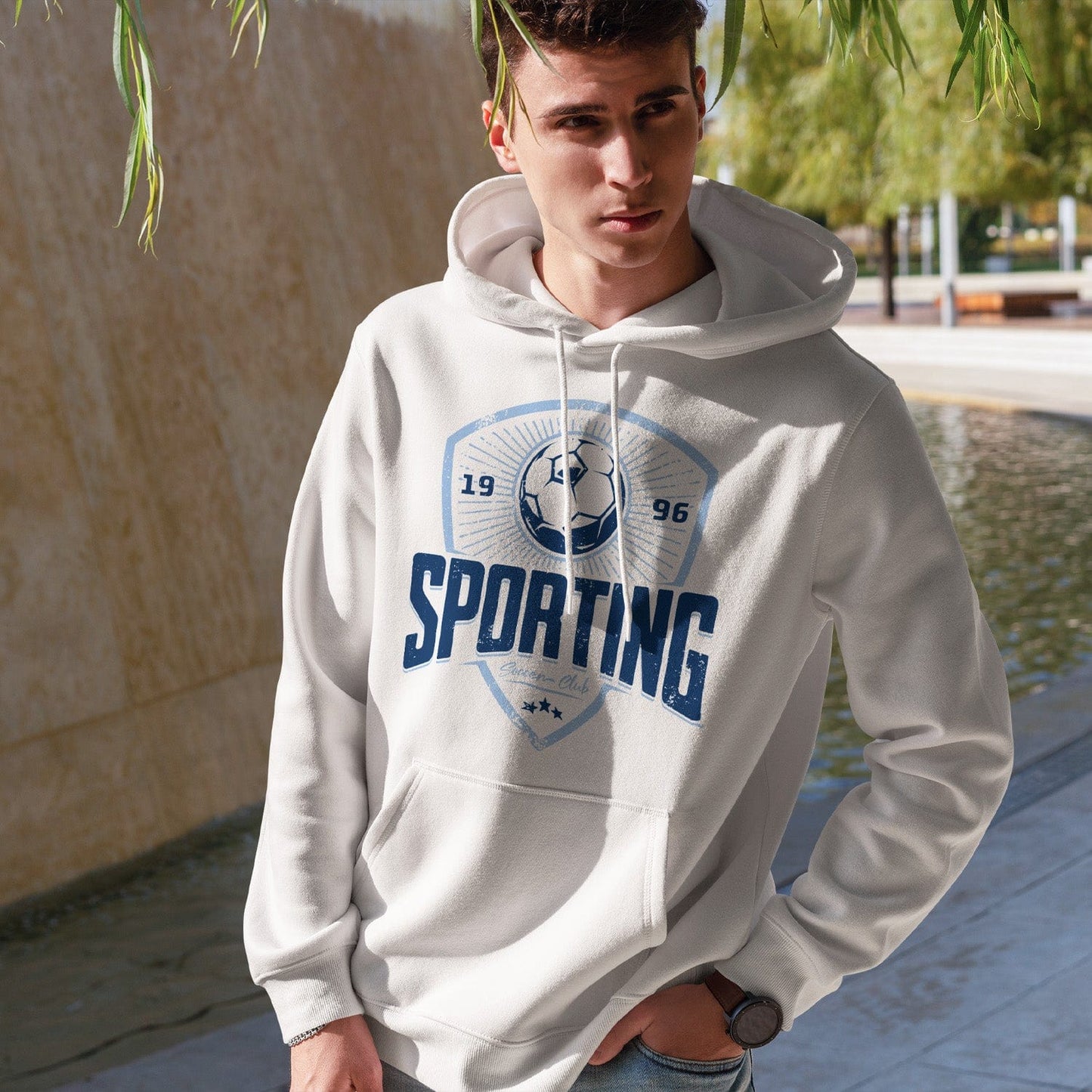 KC Swag Sporting Kansas City navy, powder SPORTING CLUB on white fleece pullover hoodie worn by male model standing near stone wall in public park