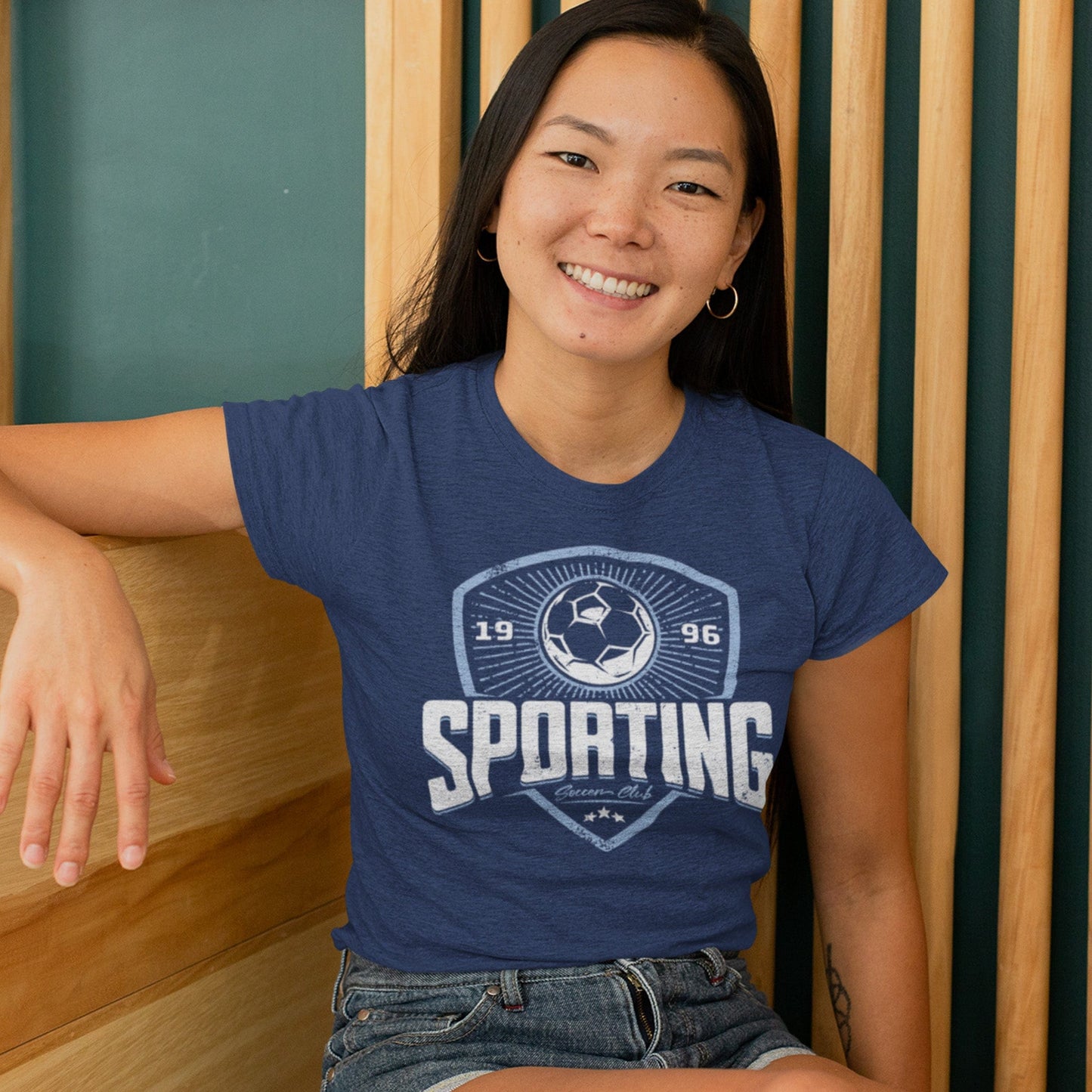 on heather navy unisex t-shirt worn by female model sitting in front of wood slat wall