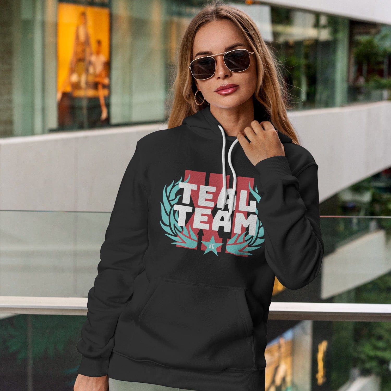 KC Swag Kansas City Current TEAL TEAM XI on black fleece pullover hoodie worn by female model in shopping mall