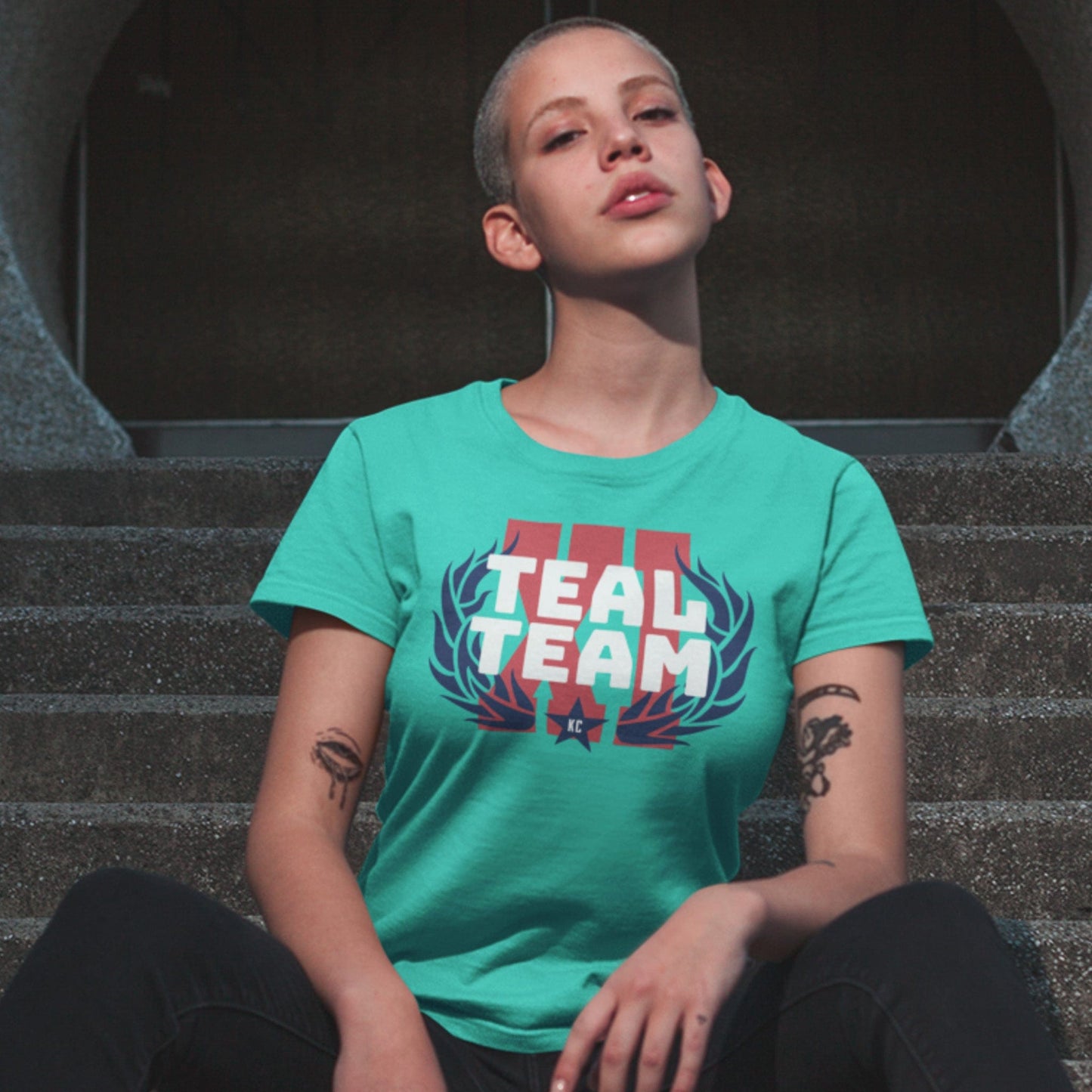 KC Swag Kansas City Current TEAL TEAM X! on teal unisex t-shirt worn by female model sitting on concrete stairs