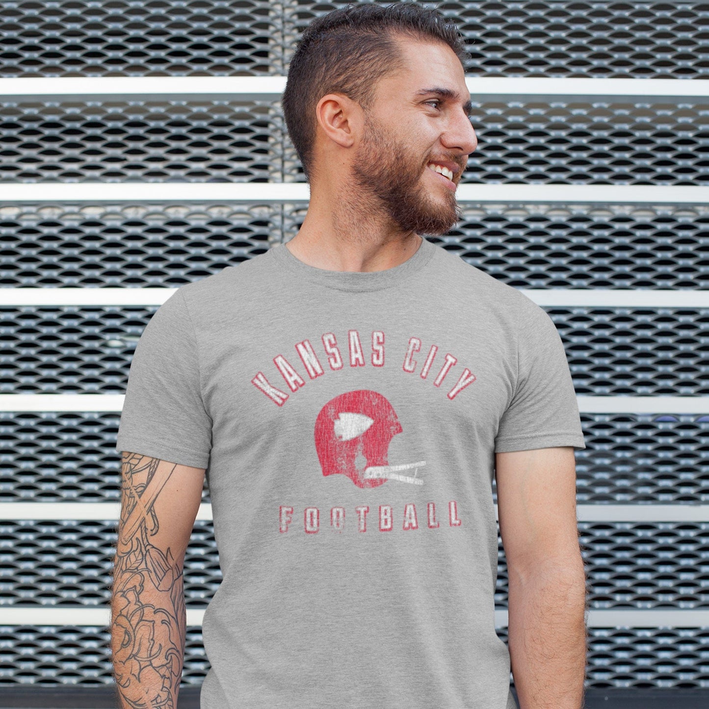 KC Swag Kansas City Chiefs red/white KANSAS CITY FOOTBALL with vintage helmet graphic on athletic heather grey t-shirt worn by male model in front of metal fence