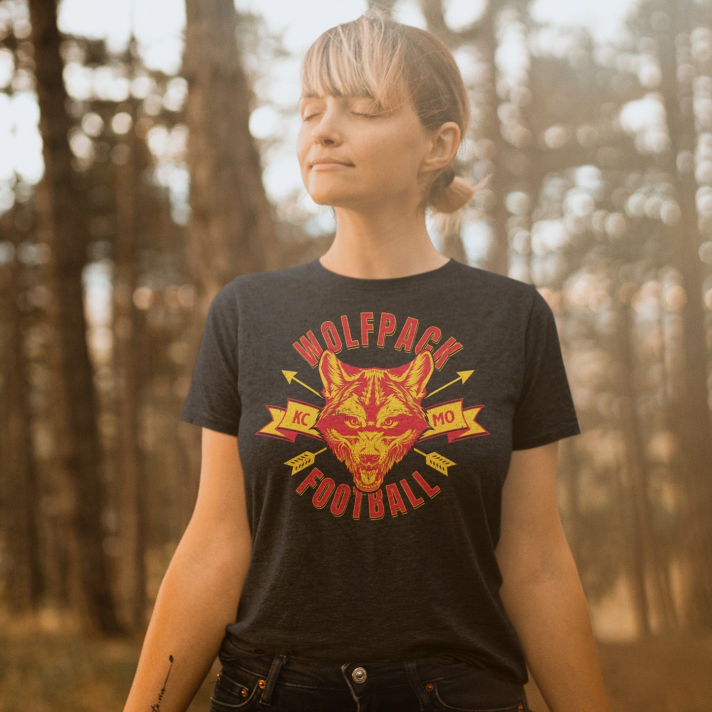 KC Swag Kansas City Chiefs WOLFPACK FOOTBALL with wolf head graphic on dark heather grey t-shirt worn by female model in warm forest setting