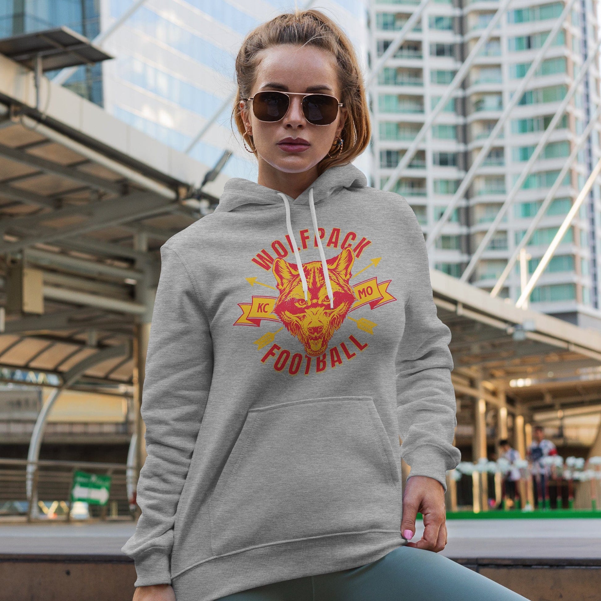 KC Swag Kansas City Chiefs WOLFPACK FOOTBALL on athletic heather grey fleece pull-over hoodie worn by female model in front of downtown buildings