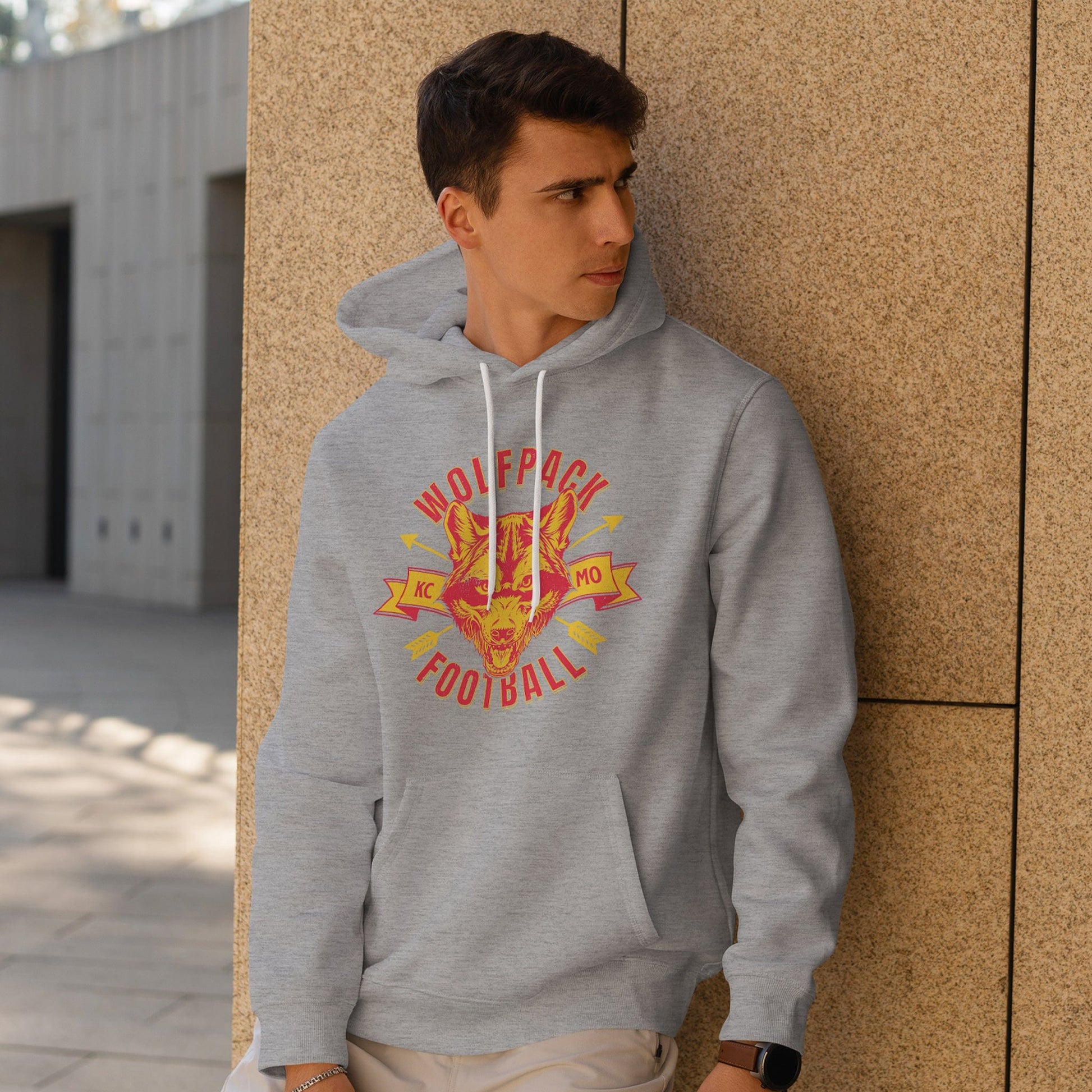 KC Swag Kansas City Chiefs WOLFPACK FOOTBALL on athletic heather grey fleece pull-over hoodie worn by male model leaning against stone wall in outdoor plaza
