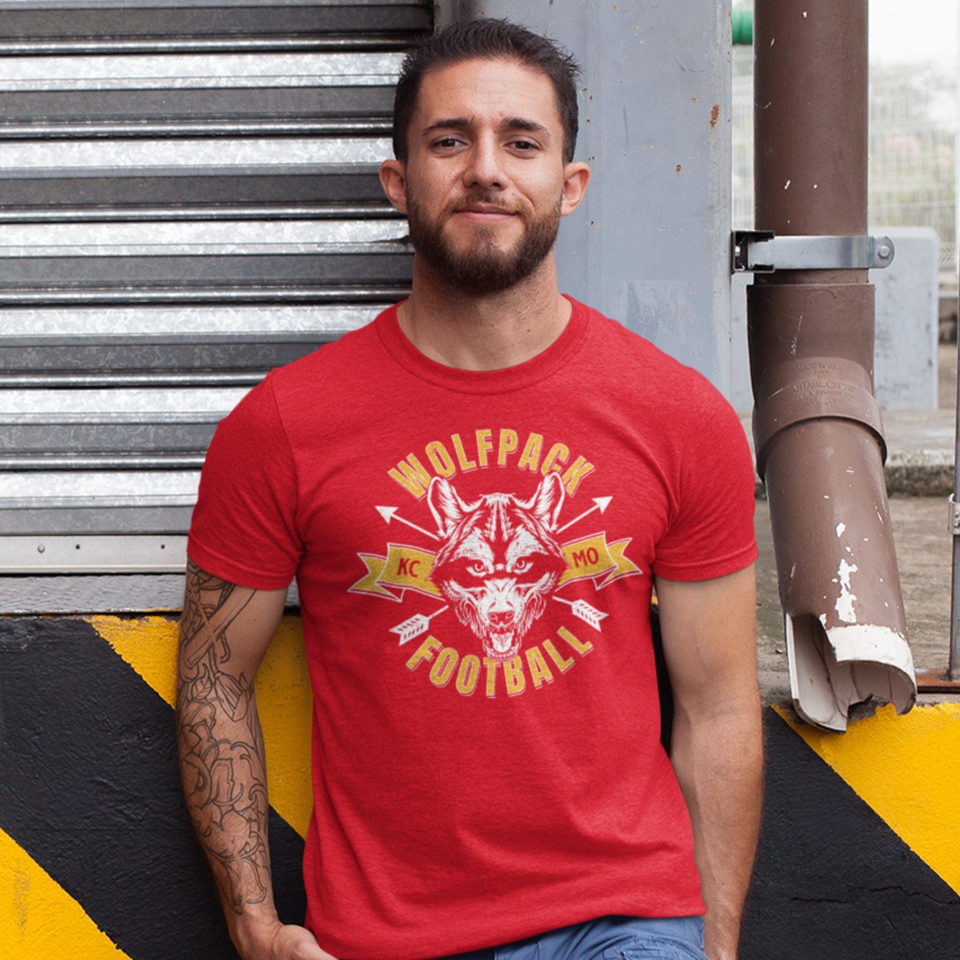 KC Swag Kansas City Chiefs WOLFPACK FOOTBALL with wolf head graphic on heather red t-shirt worn by male model leaning against urban loading dock