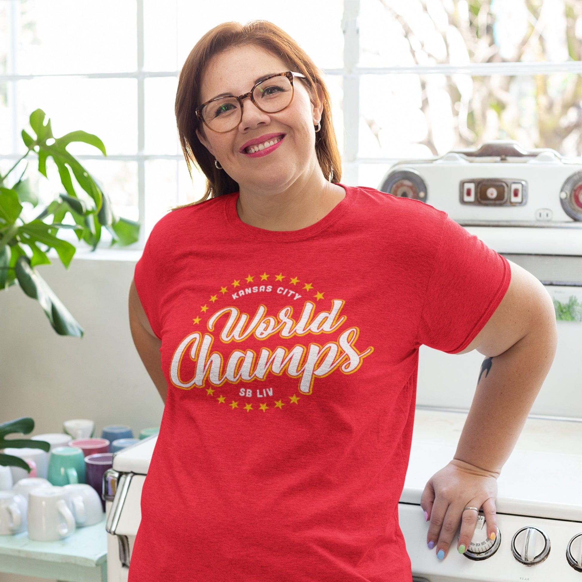 KC Swag Kansas City Chiefs yellow/white WORLD CHAMPS set in ring of stars on heather red t-shirt worn by female model in bright kitchen